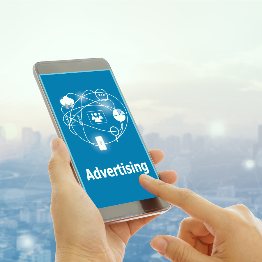 Person hält ein Smartphone in der Hand, auf dem der Schriftzug „Advertising“ sowie verschiedene Symbole für digitale Werbung (wie Diagramme, Netzwerkverbindungen und Nutzer-Icons) angezeigt werden; im Hintergrund eine verschwommene Stadtansicht.