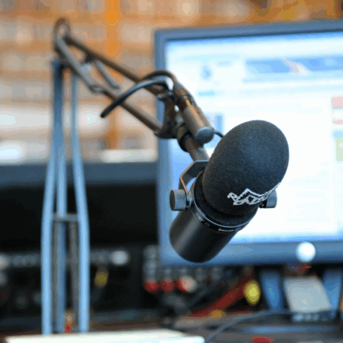 Ein professionelles Studiomikrofon an einem Schwenkarm vor einem Computerbildschirm in einem Radiostudio.